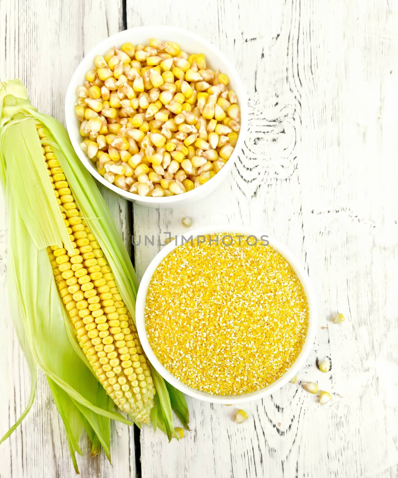 Corn grits and grains in two bowls, cob on the background of the wooden planks on top
