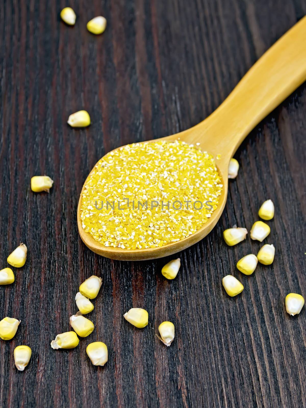 Corn grits in a spoon, corn grains on the background of wooden boards