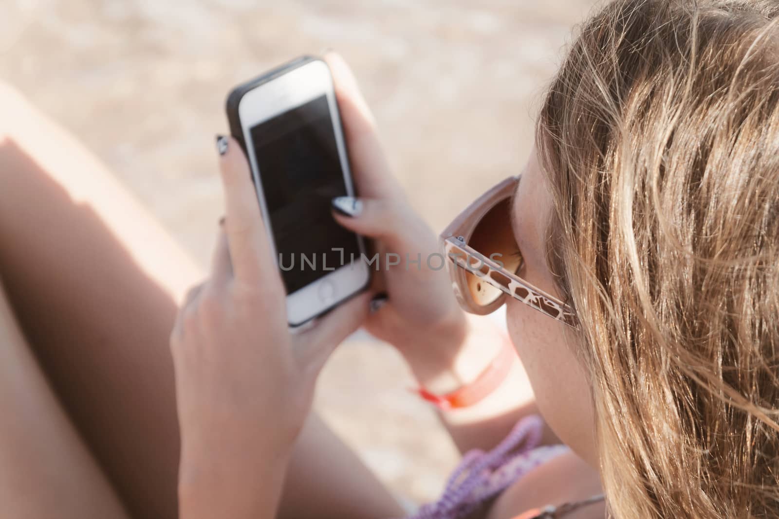 A young tanned woman looks into a smartphone through sunglasses on a lounger. The concept of a lifestyle is always on the Internet.