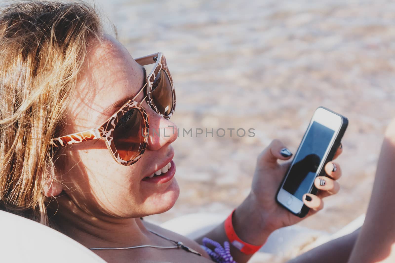 A young tanned woman looks and laughs into a smartphone through  by Tanacha