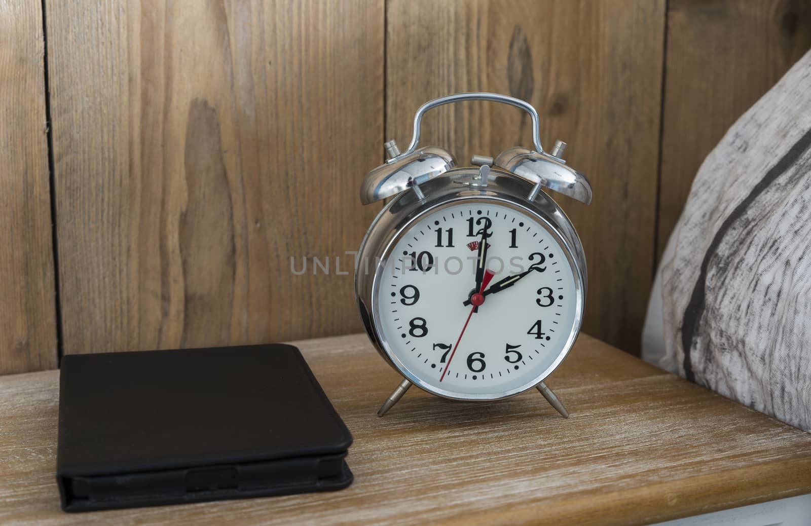 An old fashioned silver coloured bed side analogue pre digital alarm clock and modern ereader on bedside table