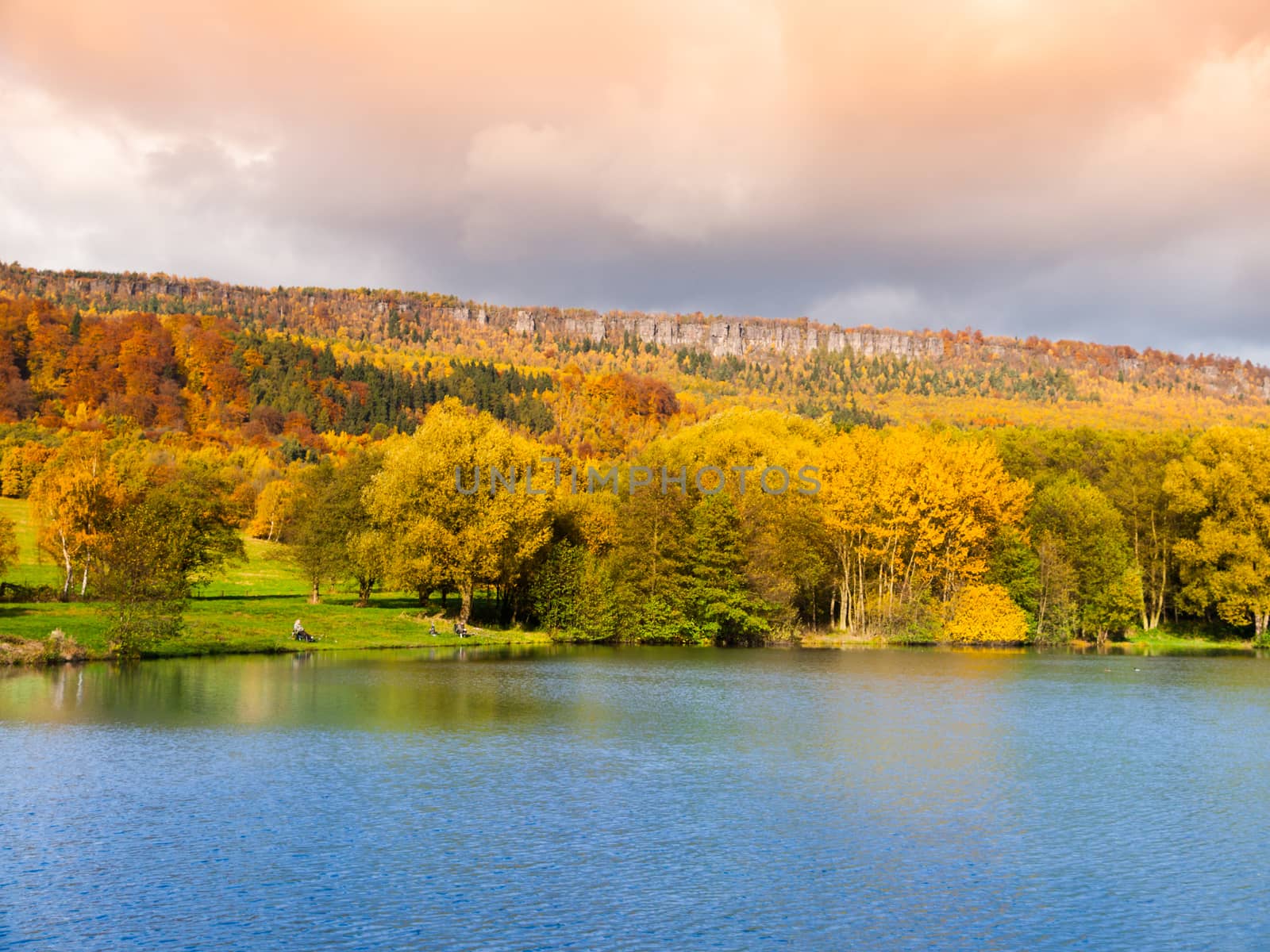 Sandstone rock formation in the middle of colorful autumn forest. Water surface on the foreground. Dramatic evening view. Tisa Rocks, aka Tiske Walls, Czech-Saxon Switzerland, Czech Republic