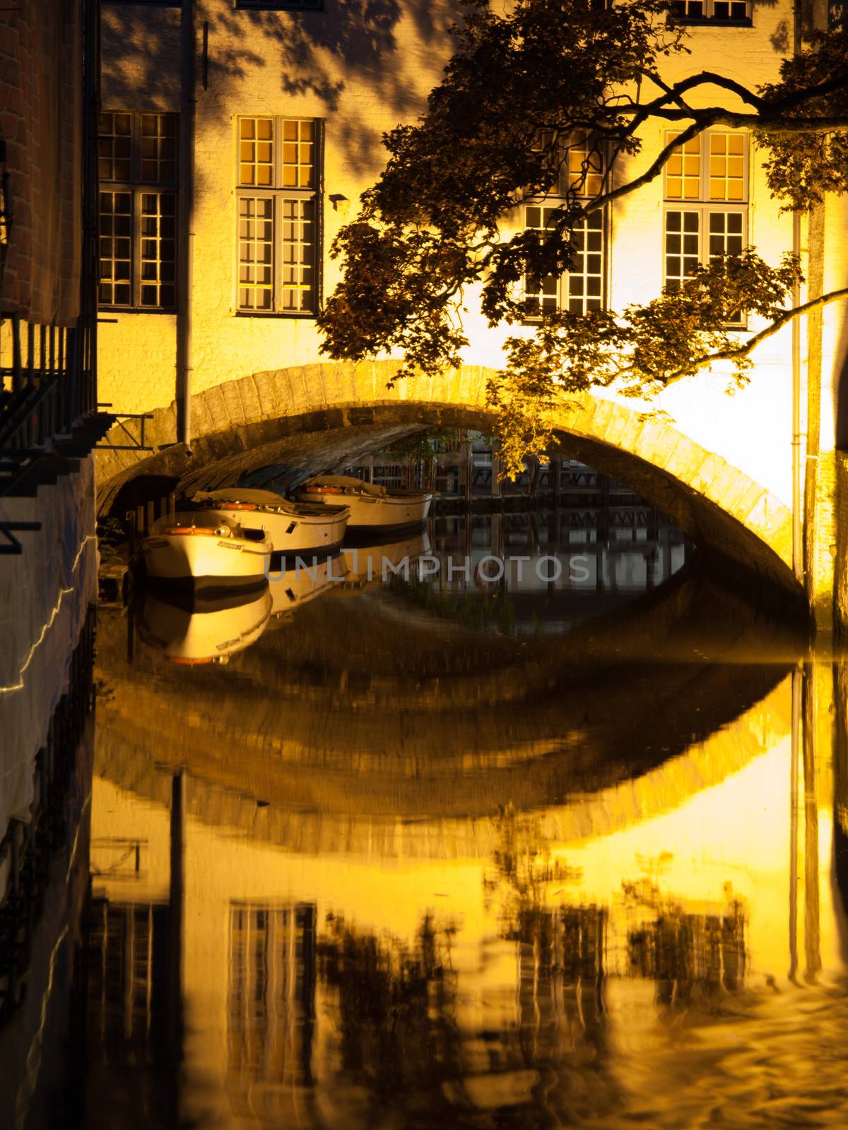 Boat reflection on water canal by night in Bruges, Belgium.