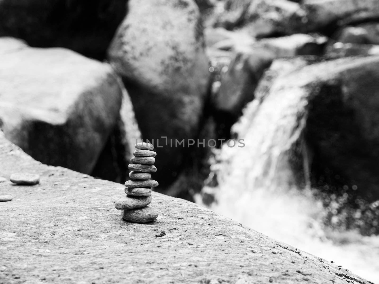 Balanced pebble stone pyramid with unfocused river waterfall on background . Black and white image.