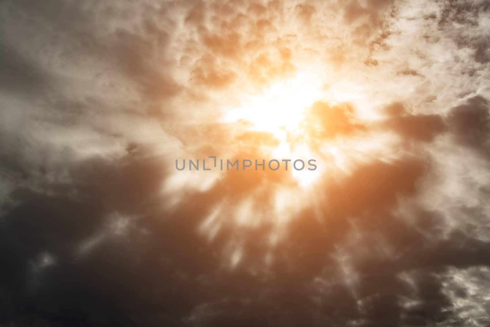 Dramatic background with warm sun rays penetrating dark clouds.