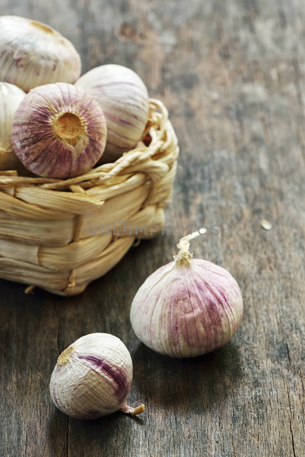 Fresh purple garlic in a small straw basket on old wooden table