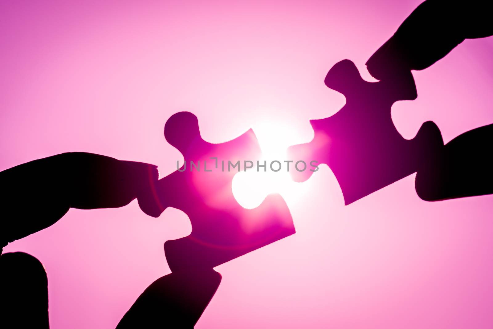 Silhouette of closeup woman's hand connecting a piece of jigsaw puzzle over sunlight effect. symbol of association and connection concept. business strategy.