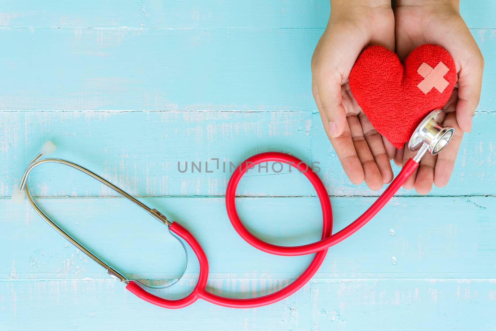 World health day, Healthcare and medical concept. Woman hand holding red heart with Stethoscope, notepad or notebook, thermometer and yellow Pill on Pastel white and blue wooden table background texture.