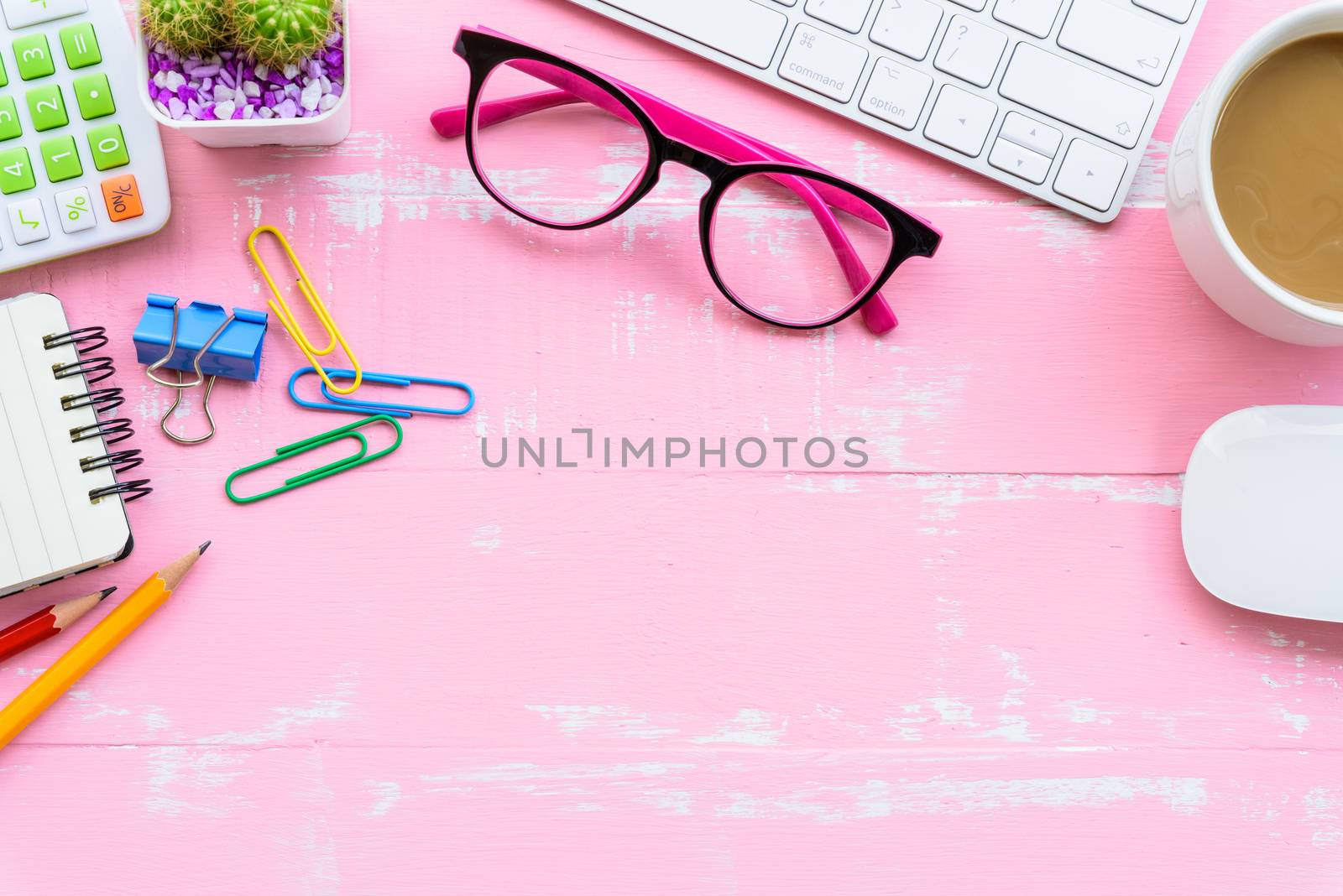 Top view office table with workspace and office accessories including calculator, mouse, keyboard, glasses, clips, flower, pen, pencil, note book, laptop and coffee on pink wooden background.