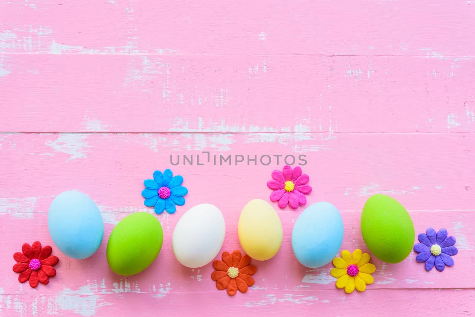 Row Easter eggs with colorful paper flowers on bright pink and white wooden background.