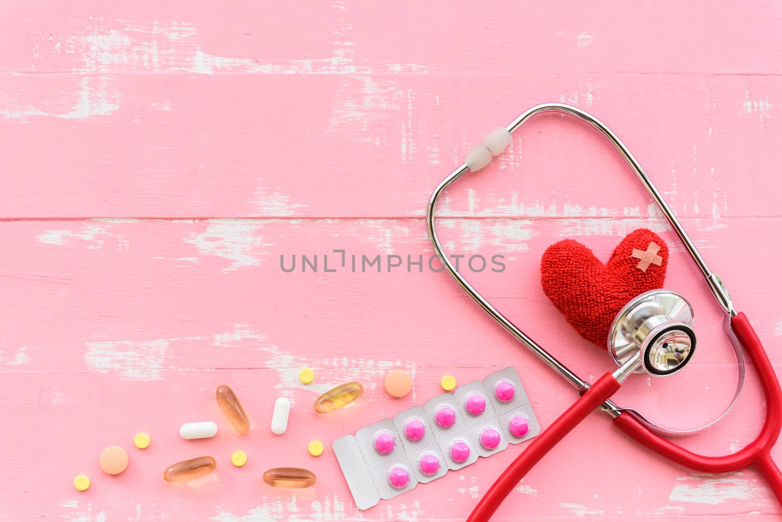 World health day, Healthcare and medical concept. Red heart with Stethoscope, notepad, thermometer and yellow Pill on Pastel white and pink wooden background.