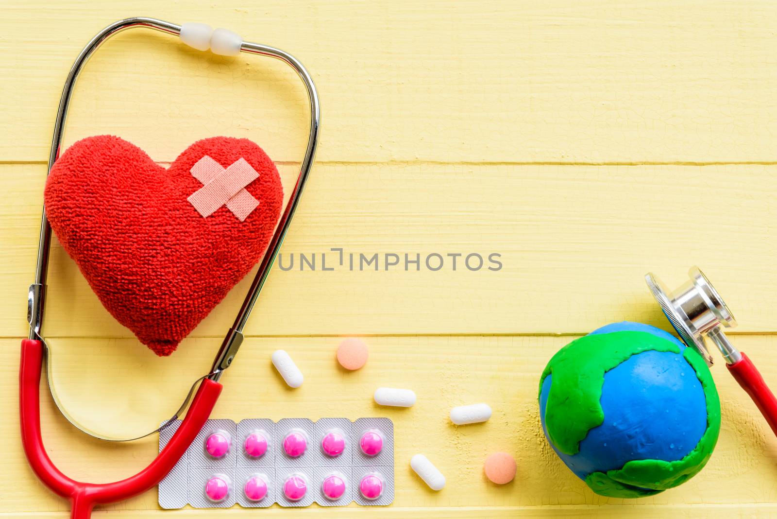 World health day, Healthcare and medical concept. Red heart with Stethoscope, handmade globe, thermometer and yellow Pill on Pastel white and pink wooden background.
