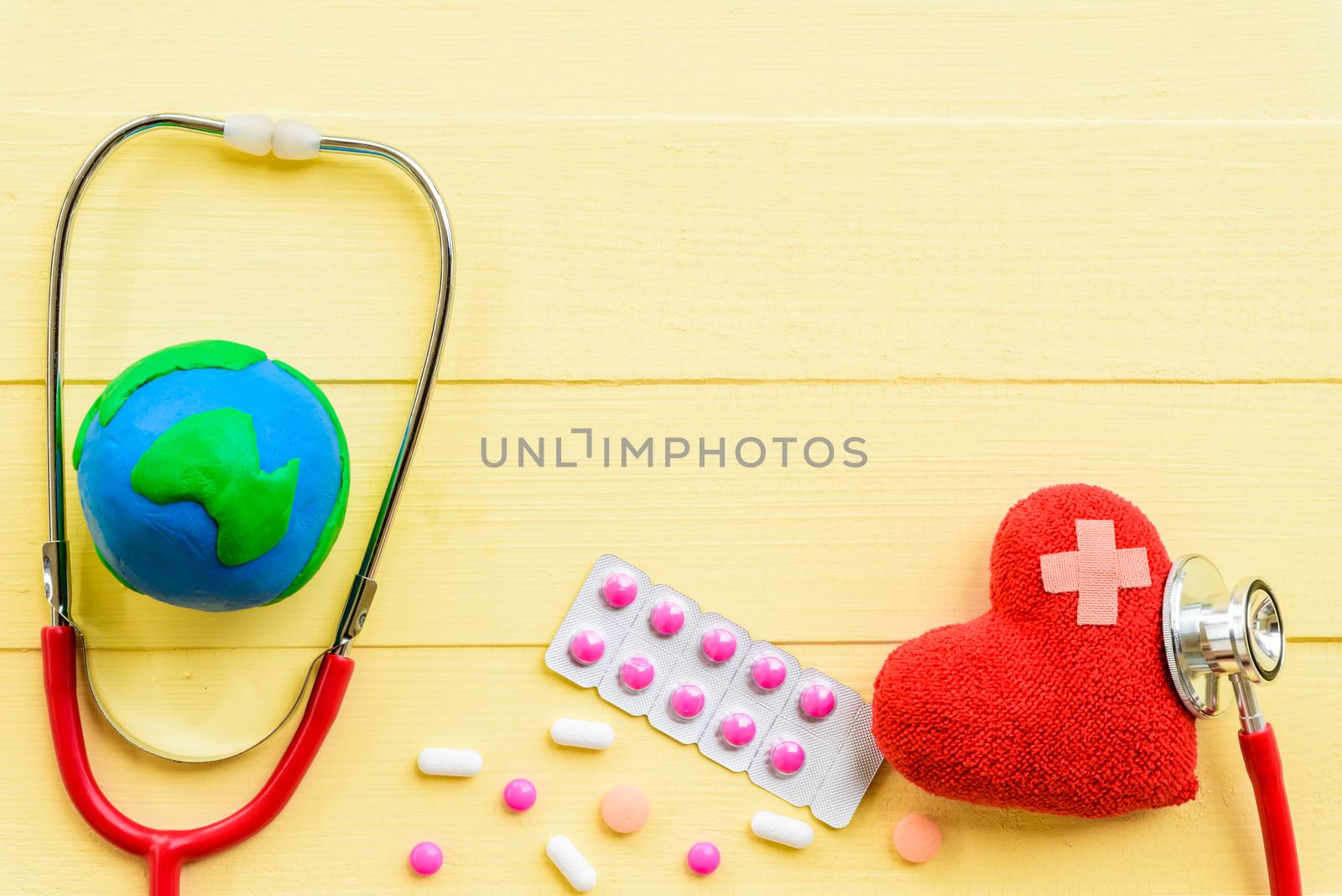 World health day, Healthcare and medical concept. Red heart with Stethoscope, handmade globe, thermometer and yellow Pill on Pastel white and pink wooden background.