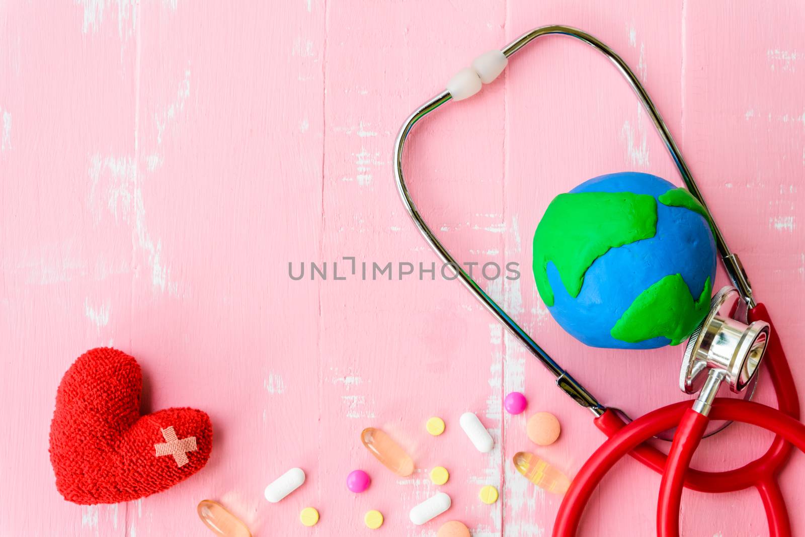 World health day, Healthcare and medical concept. Red heart with Stethoscope, handmade globe, thermometer and yellow Pill on Pastel white and pink wooden background.