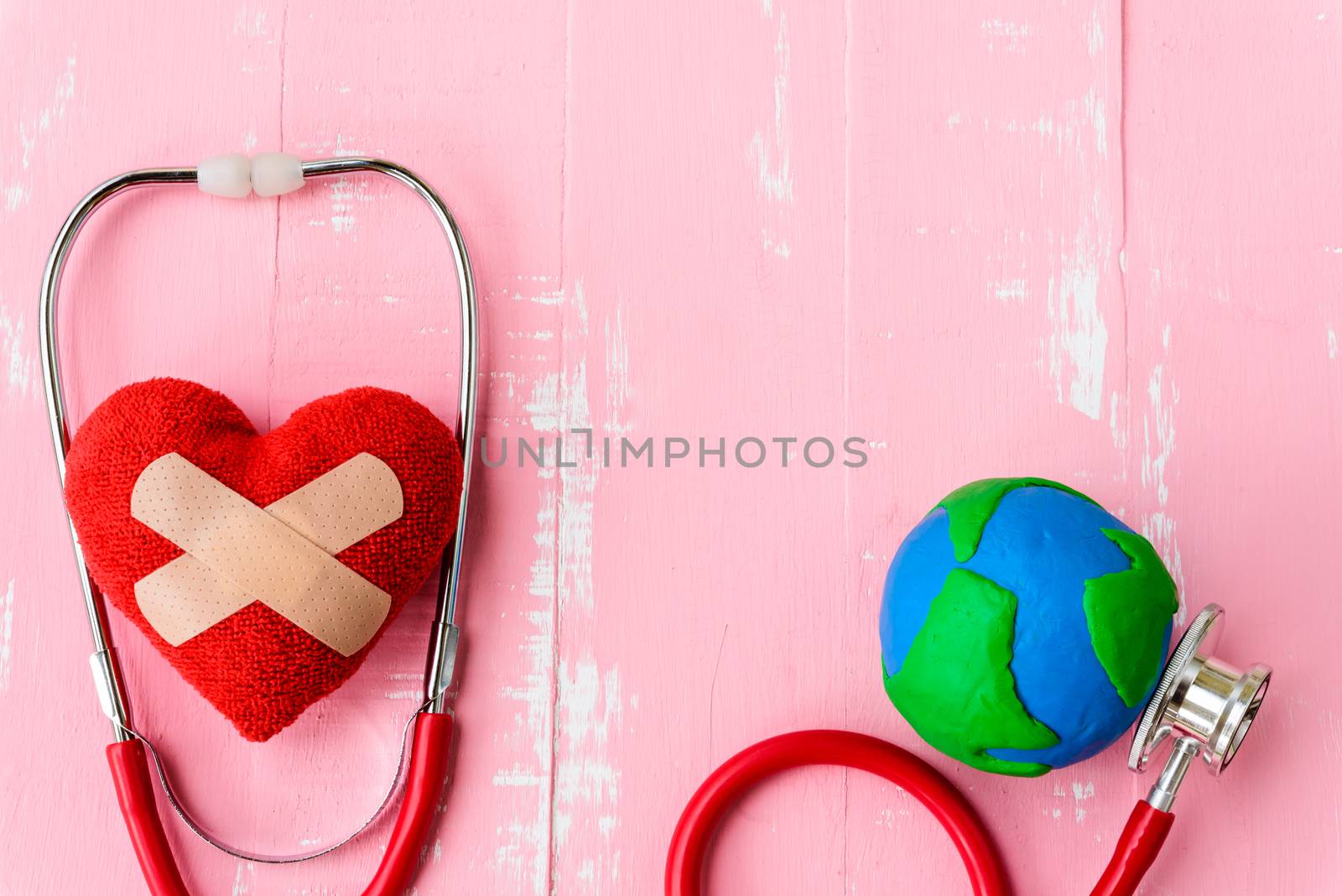 World health day, Healthcare and medical concept. Red heart with Stethoscope, handmade globe, thermometer and yellow Pill on Pastel white and pink wooden background.