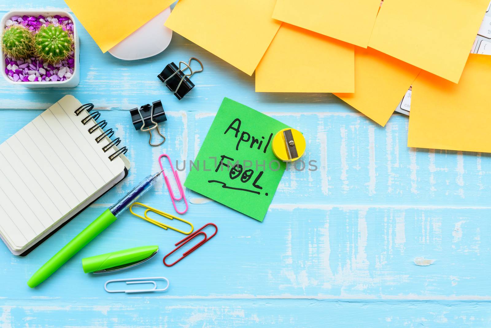 April fool's day celebration concept. office table with office accessories laptop, keyboard, mouse covered in sticky notes  on blue wooden background.