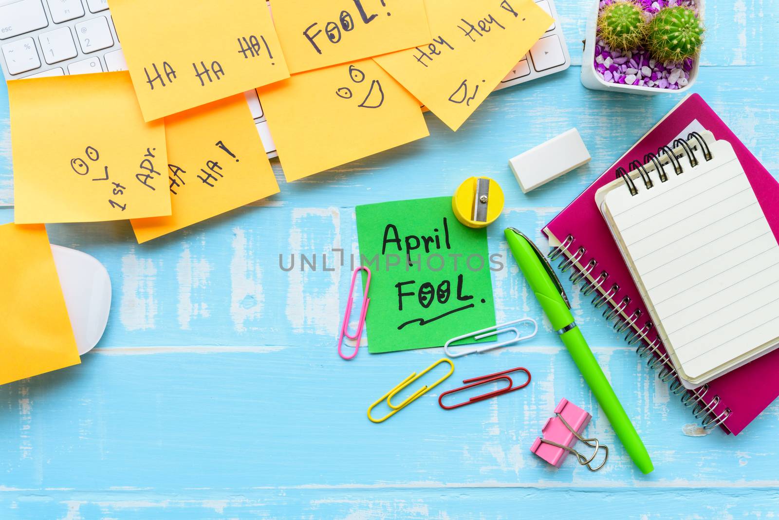 April fool's day celebration concept. office table with office accessories laptop, keyboard, mouse covered in sticky notes  on blue wooden background.