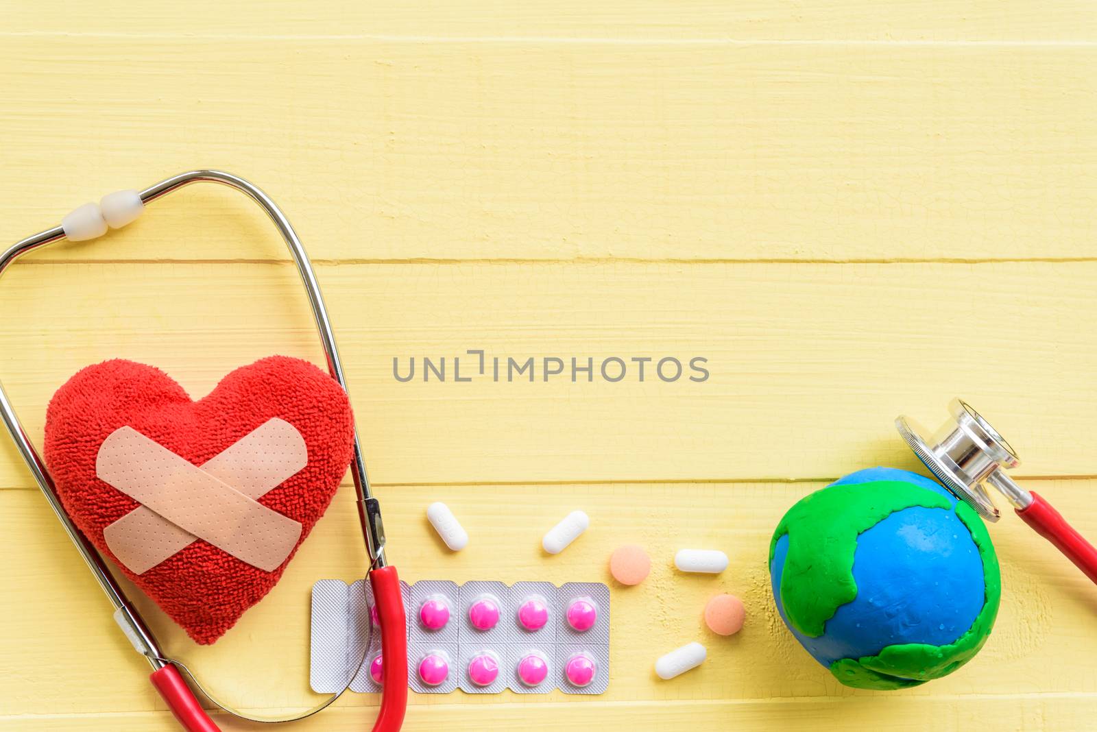 World health day, Healthcare and medical concept. Red heart with Stethoscope, handmade globe, thermometer and yellow Pill on Pastel white and pink wooden background.