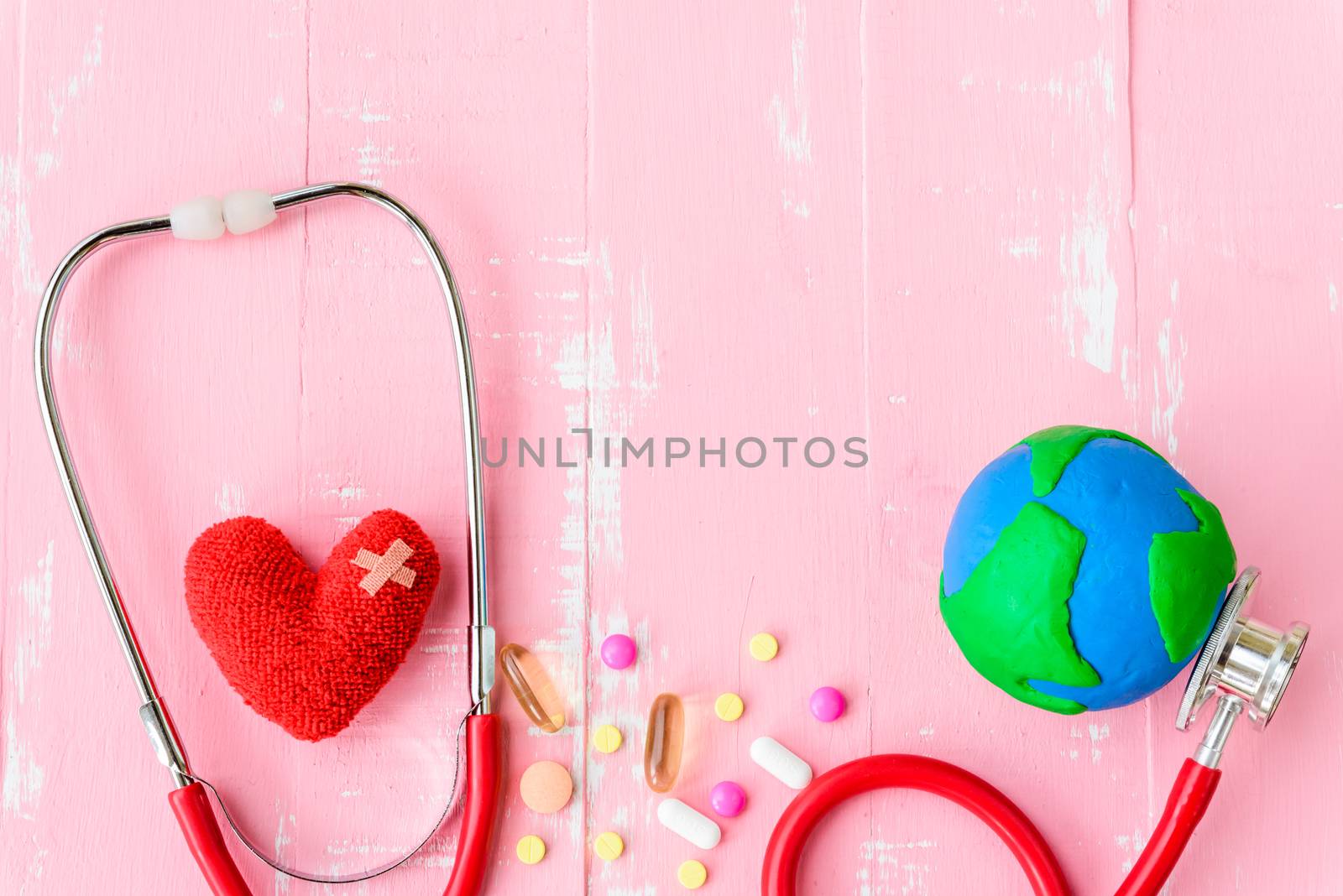World health day, Healthcare and medical concept. Red heart with Stethoscope, handmade globe, thermometer and yellow Pill on Pastel white and pink wooden background.