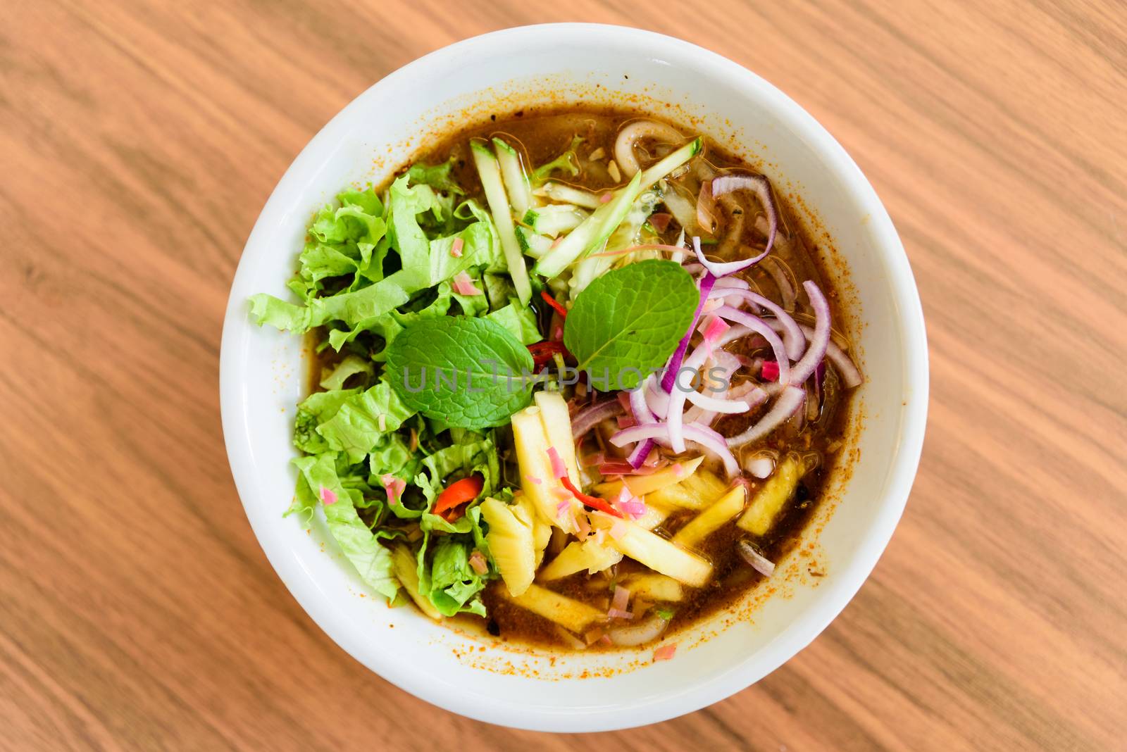 Laksa on wooden table. Laksa is a spicy noodle soup popular in the Peranakan cuisine.