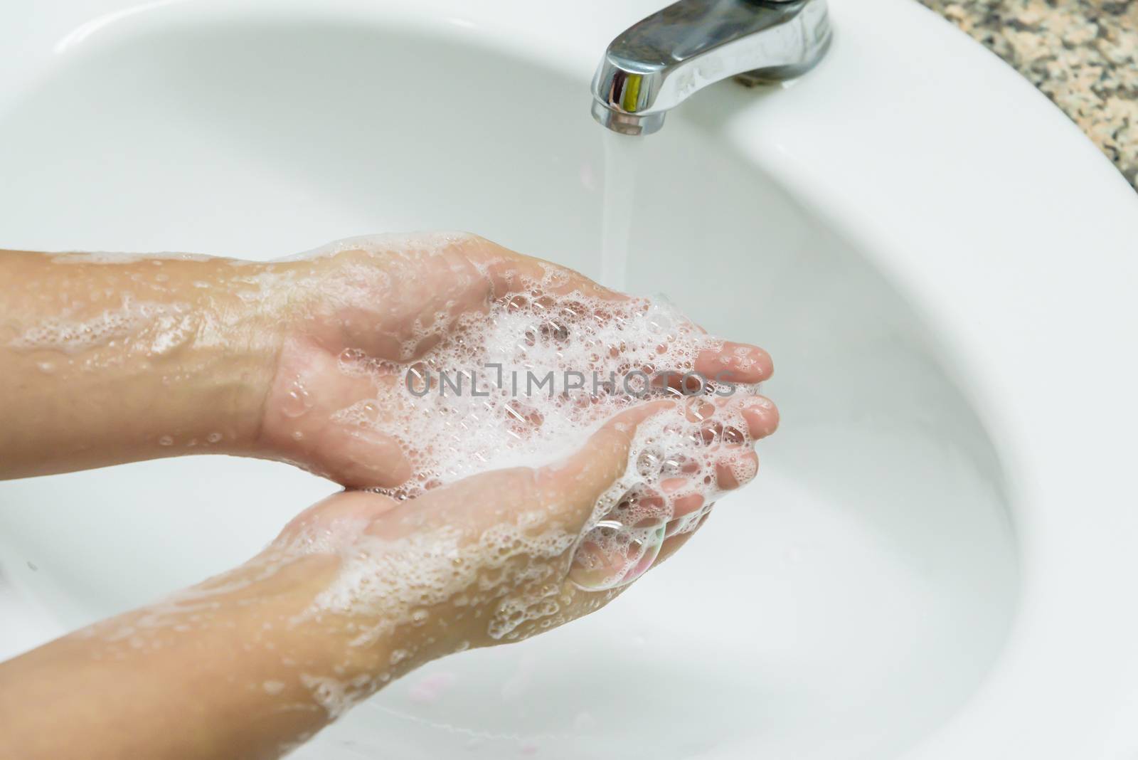 Selective focus of woman washing hands with soap under the faucet with water  in the bathroom.