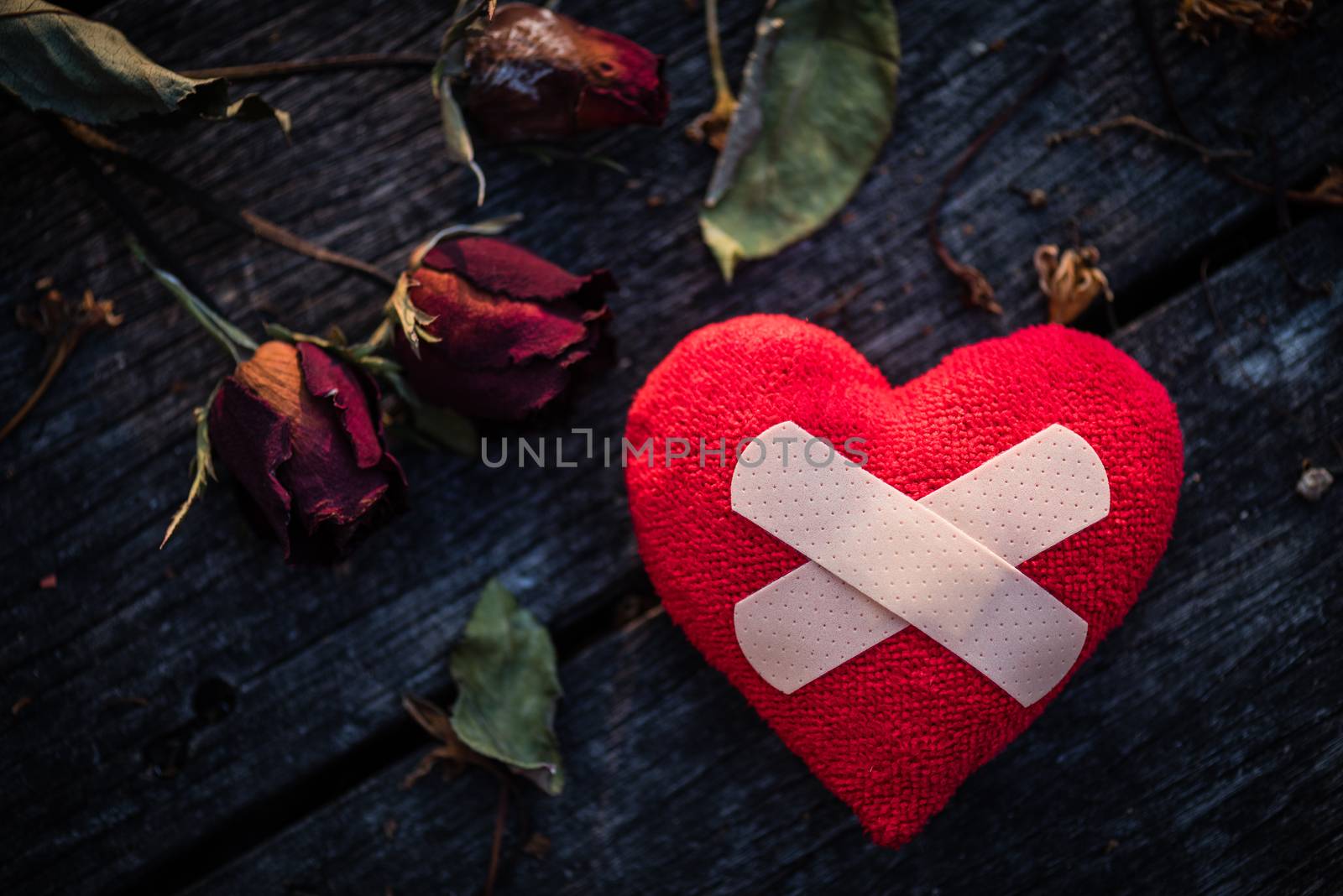 First Aid Band Cushioned Plaster Strip Medical Patch glued on red heart with dried red rose on wooden background. Heart broken, Love and Valentines day concept.