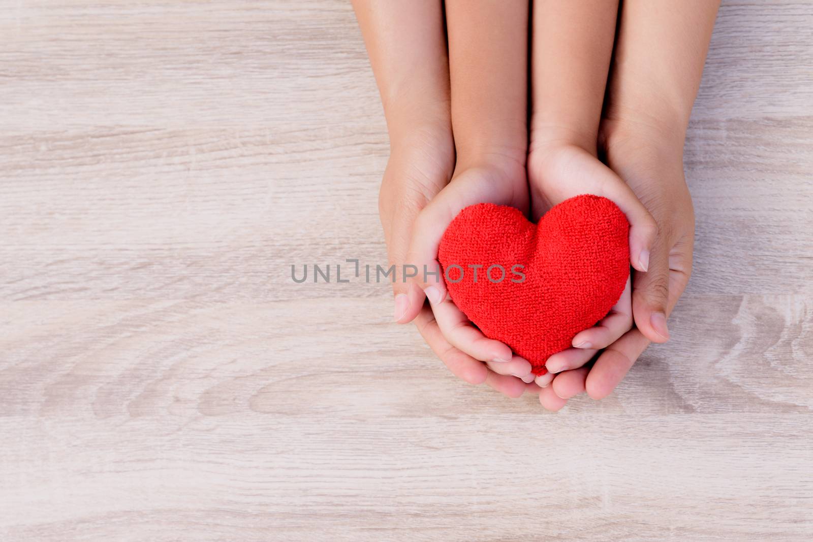 Health care, love, organ donation, family insurance and CSR concept. adult and child hands holding handmade red heart on wooden background.