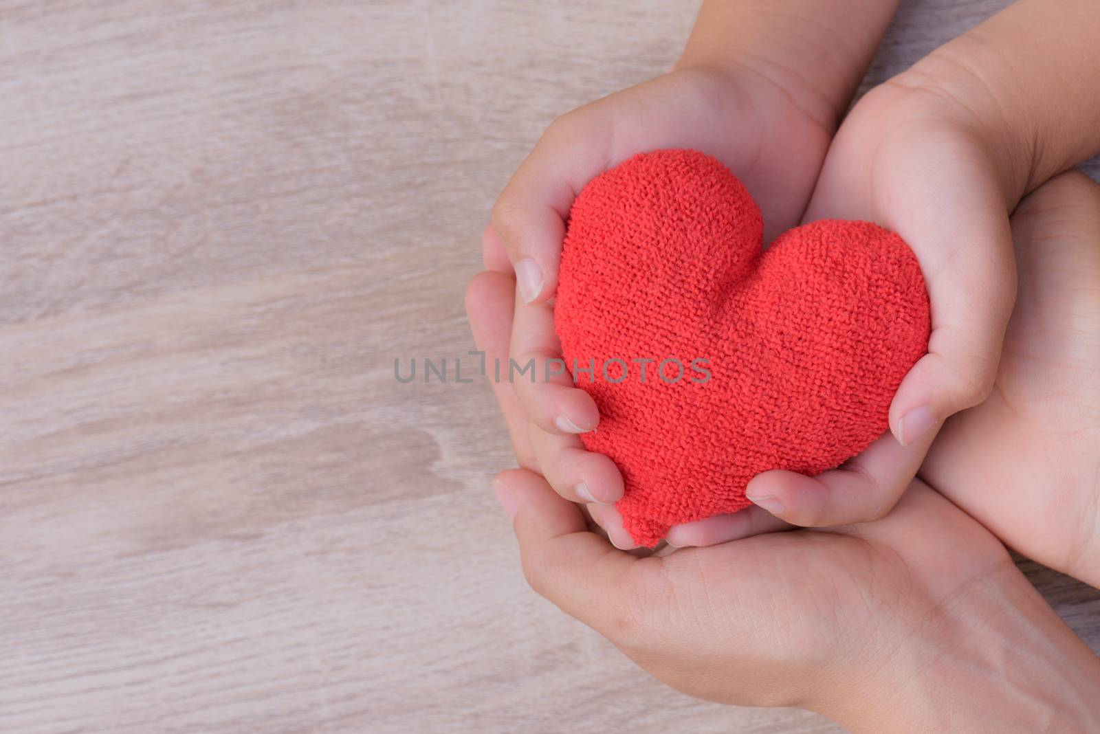 Health care, love, organ donation, family insurance and CSR concept. adult and child hands holding handmade red heart on wooden background. First Aid Band Cushioned Plaster Strip Medical Patch glued on red heart.