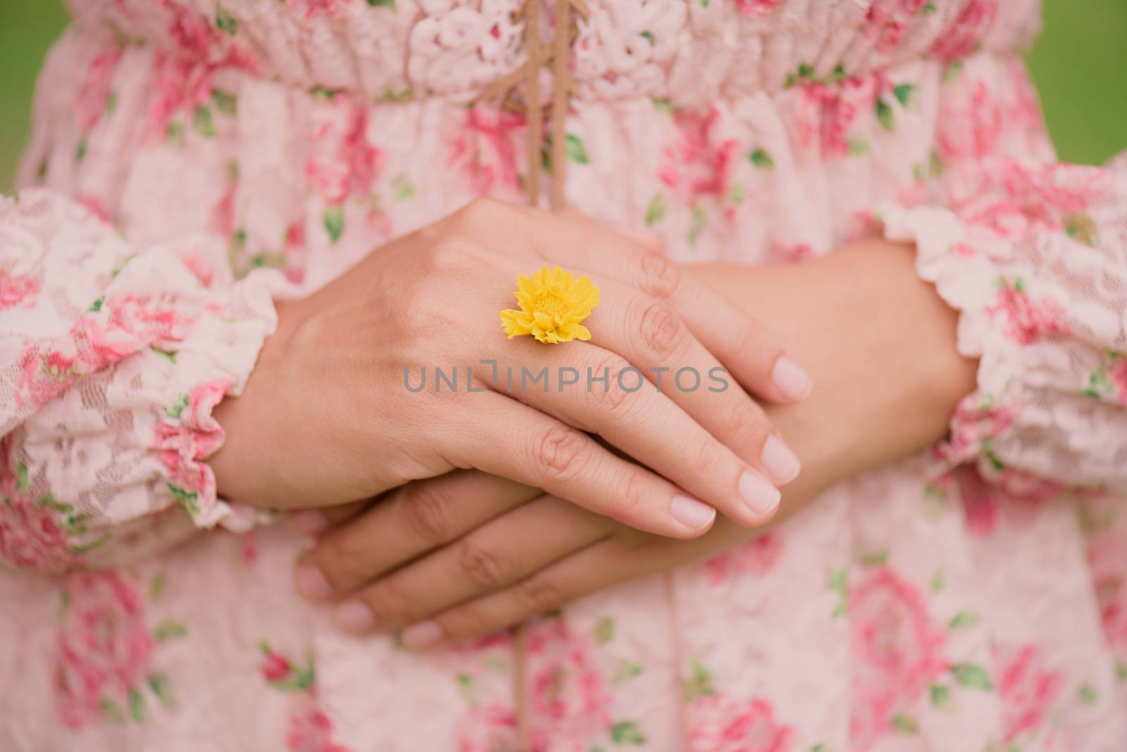 Young woman hand wearing Yellow flower represent of wedding ring on grass green background. Broken hearted, Love forever, Wedding and Valentines day concept.