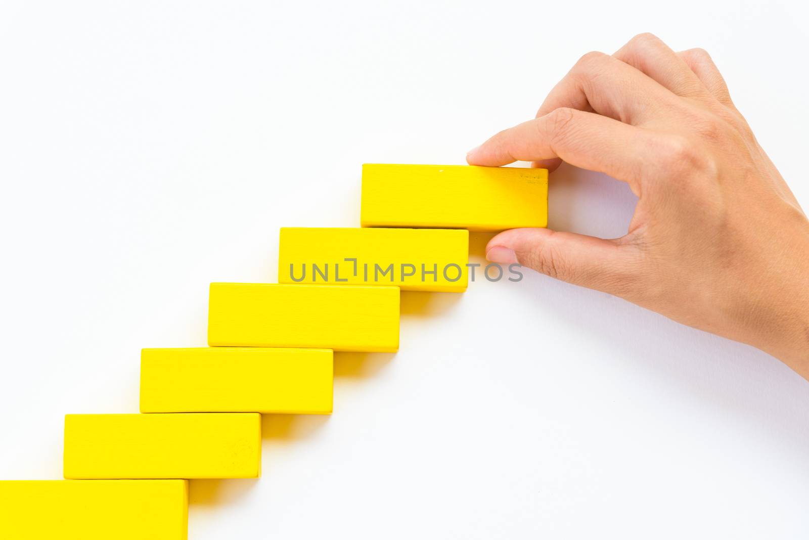 Concept of building success foundation. Women hand put red wooden block on yellow wooden blocks in the shape of a staircase