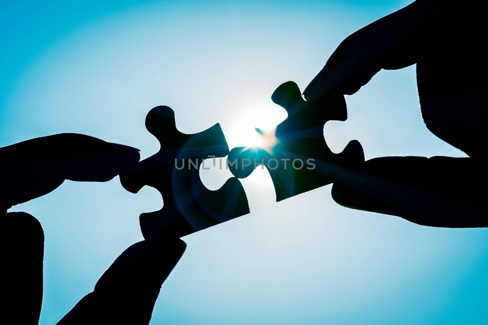 Silhouette of closeup woman's hand connecting a piece of jigsaw puzzle over sunlight effect. symbol of association and connection concept. business strategy.