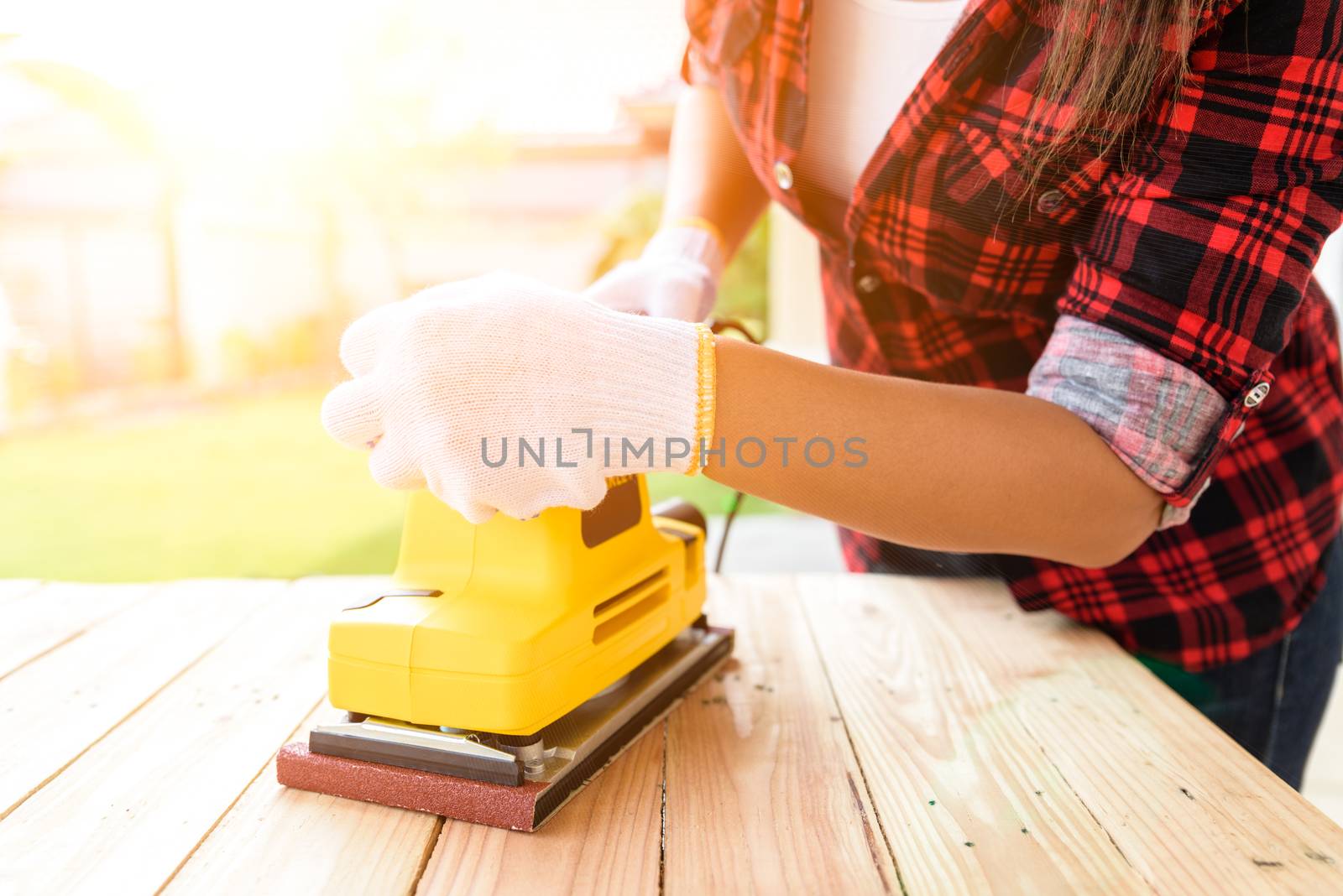 Womam Carpenter working with wood electrical sanding machine by spukkato