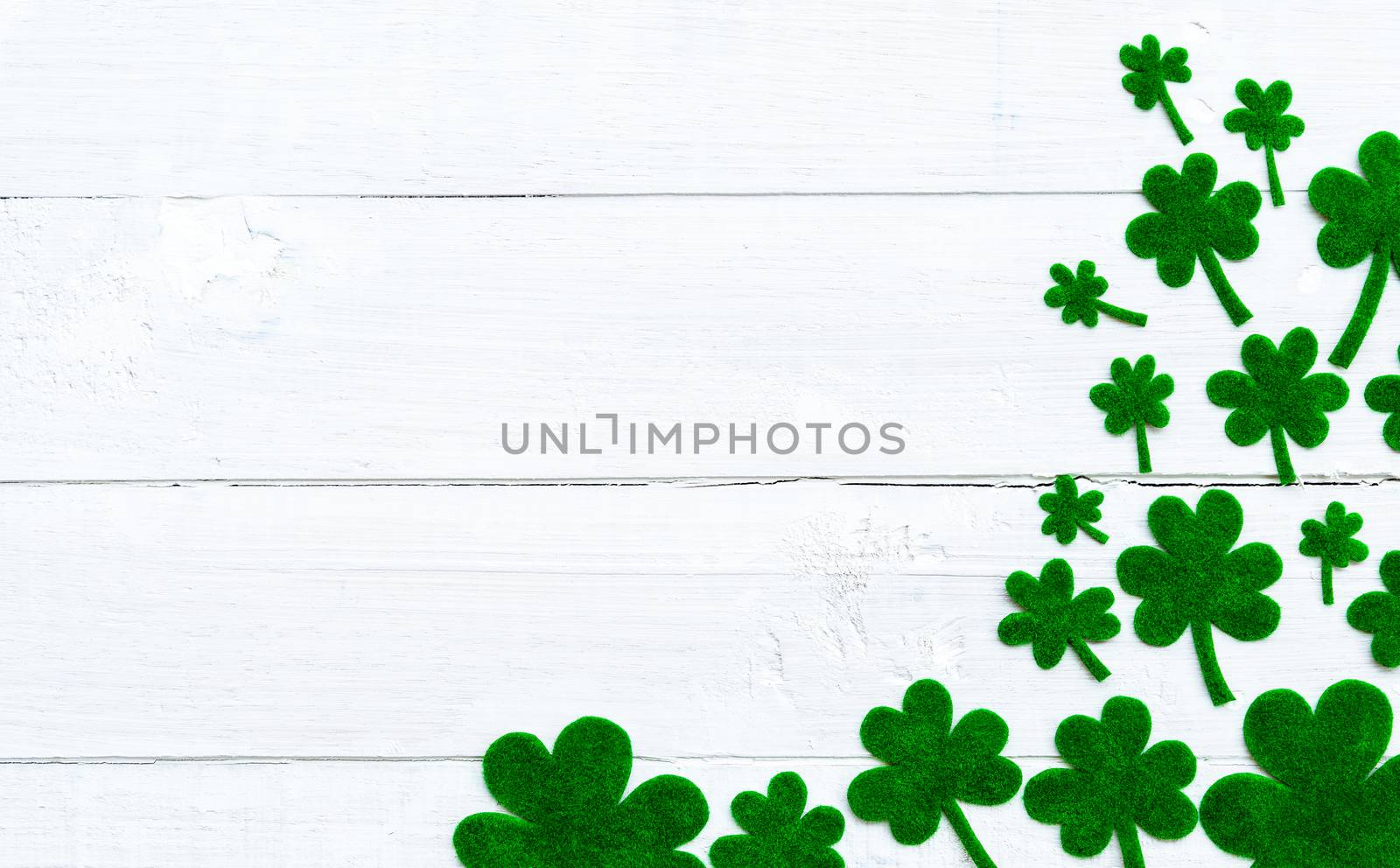 Happy St Patricks Day message and a lot of green paper clover leaf on white wooden background