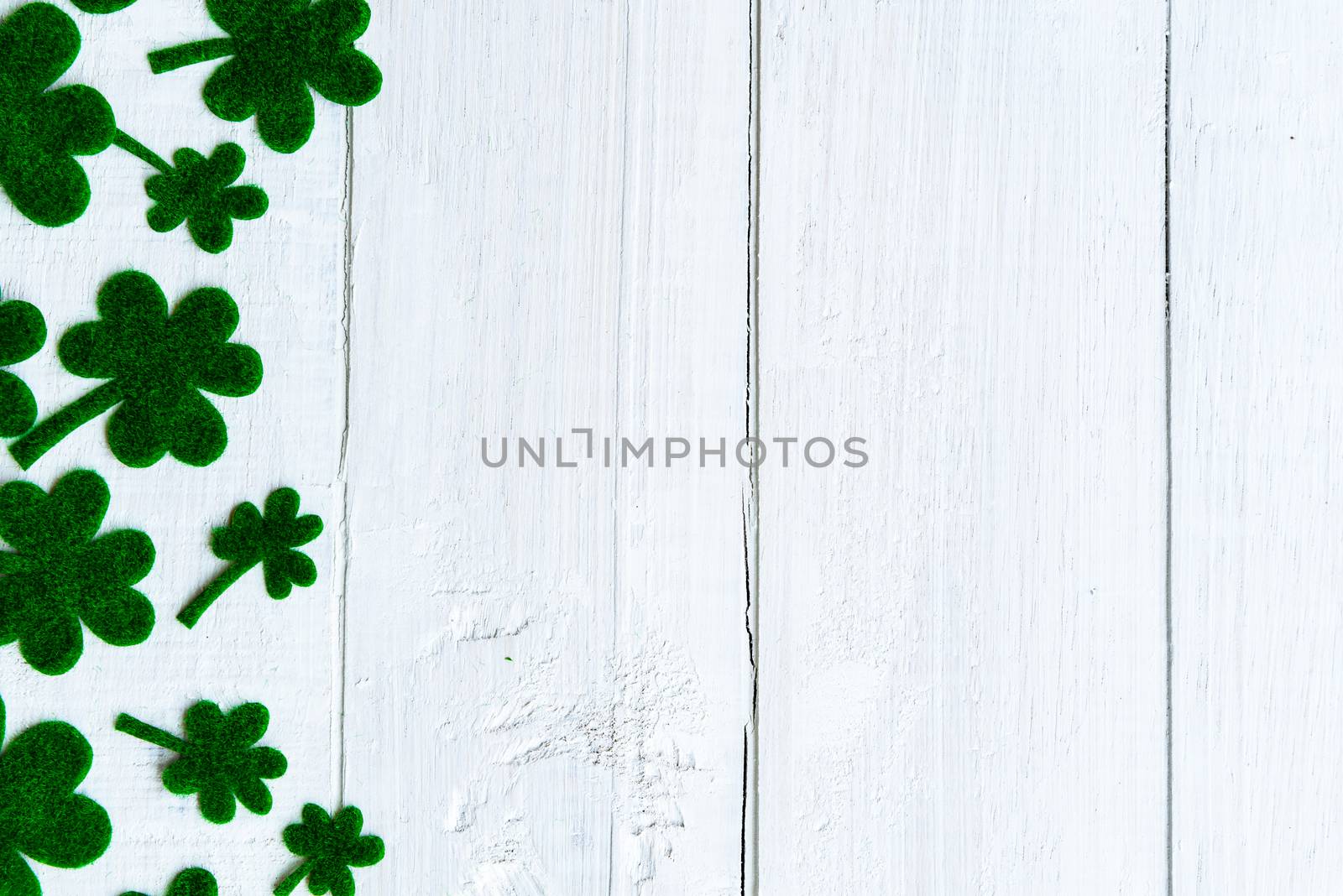 Happy St Patricks Day message and a lot of green paper clover leaf on white wooden background