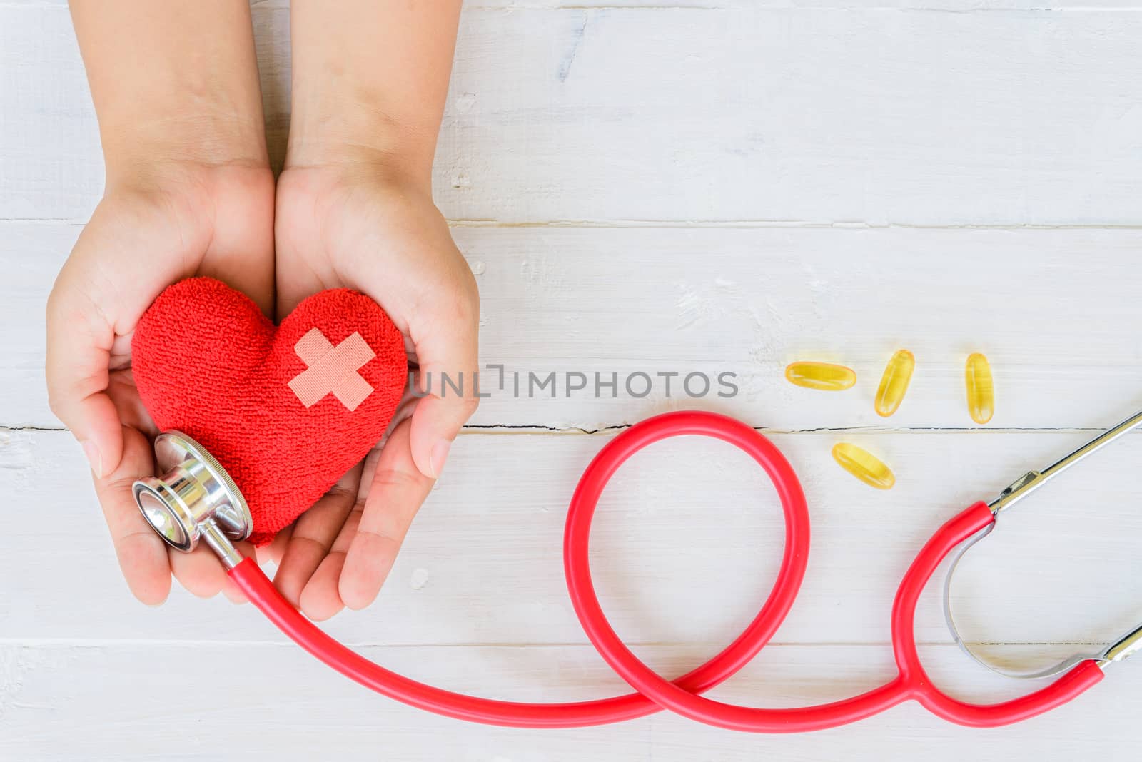 World health day, Healthcare and medical concept. Woman hand holding red heart with Stethoscope, notepad or notebook, thermometer and yellow Pill on Pastel white and blue wooden table background texture.