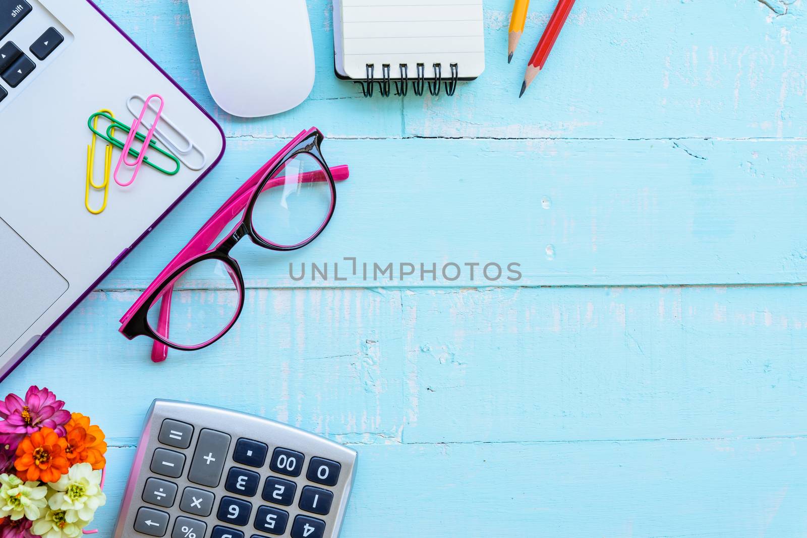Top view office table with workspace and office accessories including calculator, mouse, keyboard, glasses, clips, flower, pen, pencil , note book and laptop on bright green wooden background.