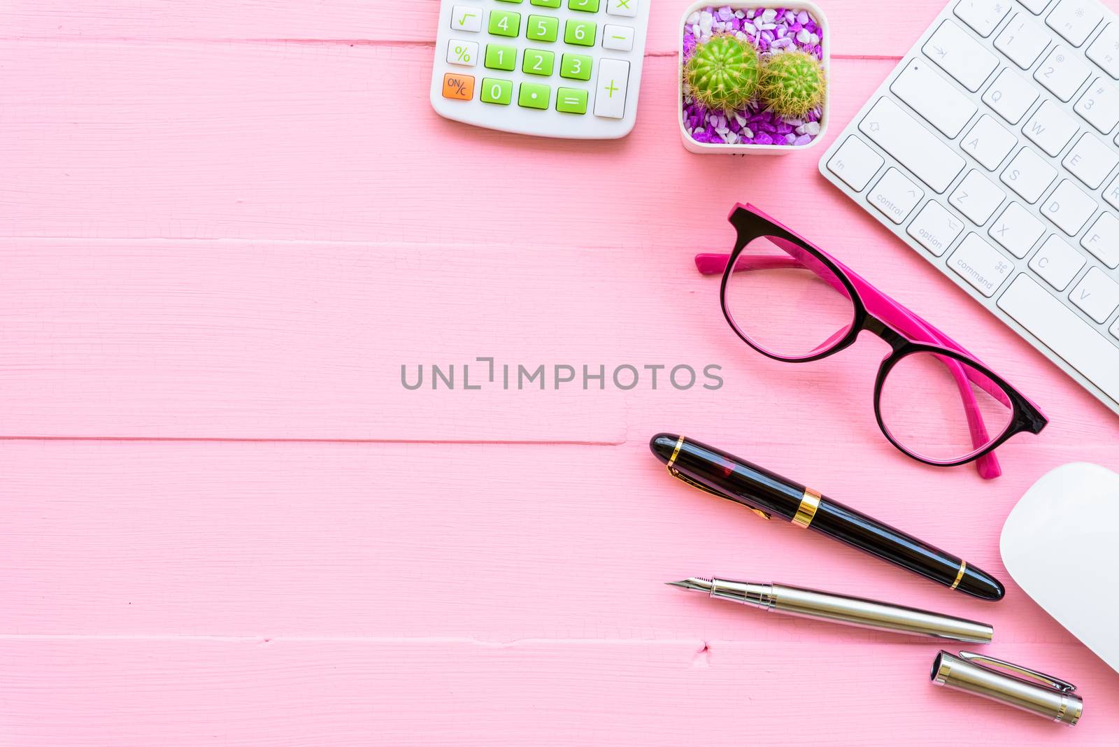 Top view office table with workspace and office accessories including calculator, mouse, keyboard, glasses, clips, flower, pen, pencil, note book, laptop and coffee on pink wooden background.