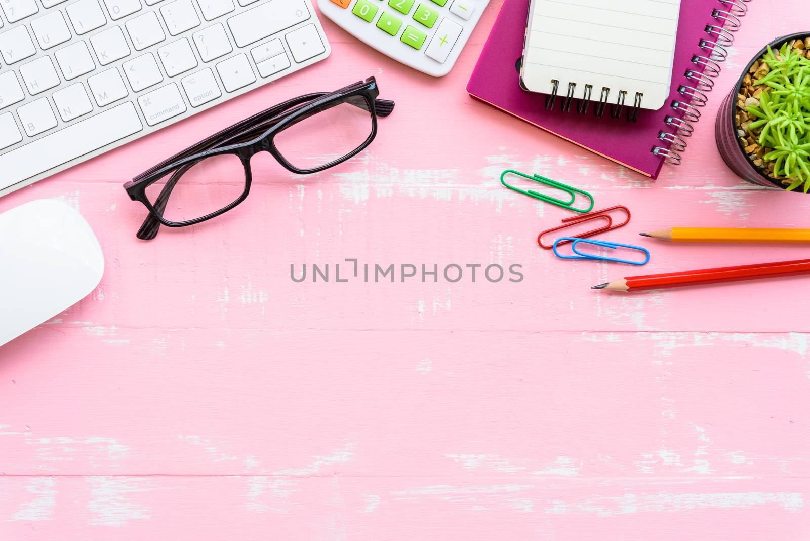 Top view office table with workspace and office accessories including calculator, mouse, keyboard, glasses, clips, flower, pen, pencil, Pencil sharpener , note book, laptop and coffee on bright pink and white wooden background.