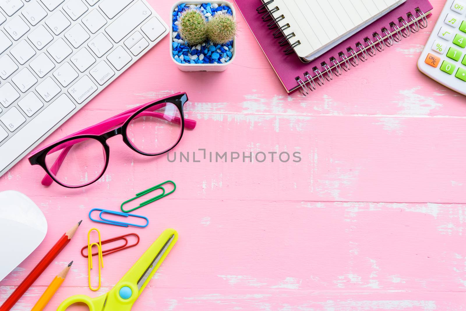 Top view office table with workspace and office accessories including calculator, mouse, keyboard, glasses, clips, flower, pen, pencil, note book, laptop and coffee on pink wooden background.