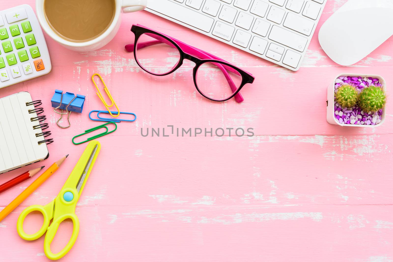 Top view office table with workspace and office accessories including calculator, mouse, keyboard, glasses, clips, flower, pen, pencil, note book, laptop and coffee on pink and white wooden background.