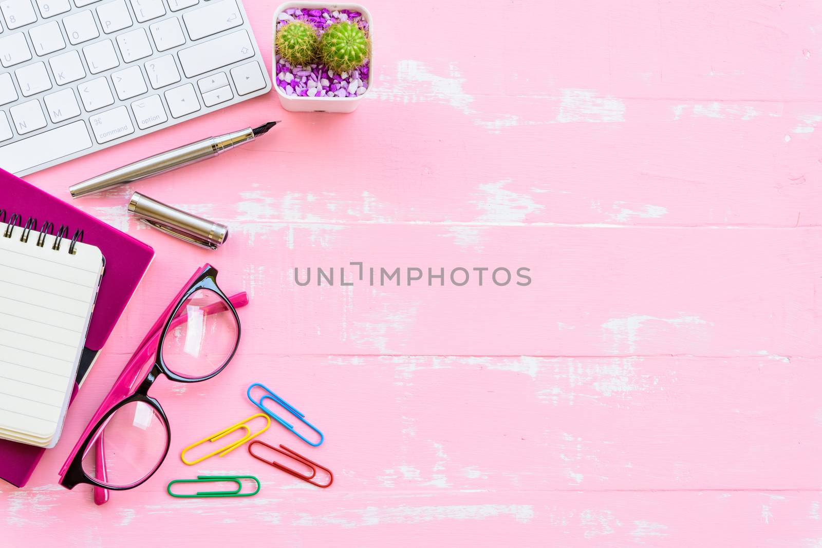 Top view office table with workspace and office accessories including calculator, mouse, keyboard, glasses, clips, flower, pen, pencil, Pencil sharpener , note book, laptop and coffee on bright pink and white wooden background.