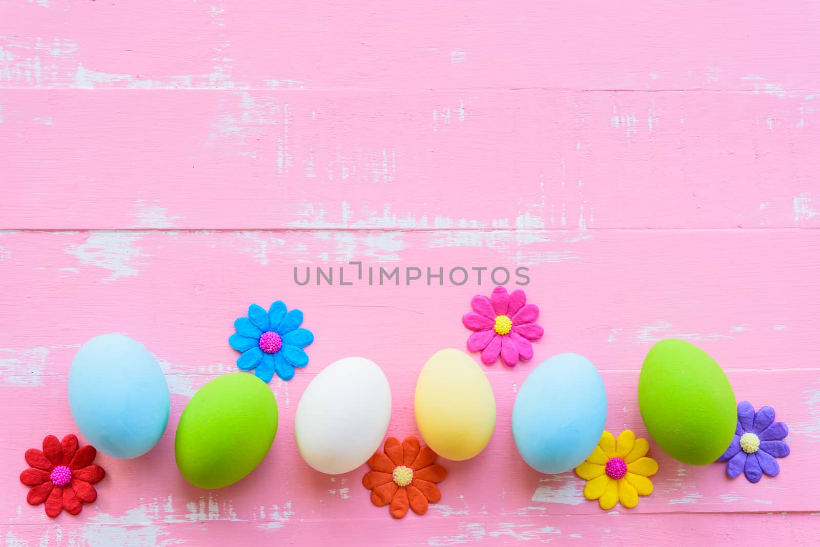 Row Easter eggs with colorful paper flowers on bright pink and white wooden background.