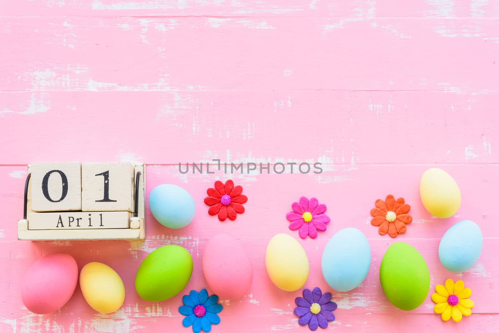 Wooden block calendar for Easter Day, April 1. Row Easter eggs with colorful paper flowers and red ribbon on bright pink and white wooden background.