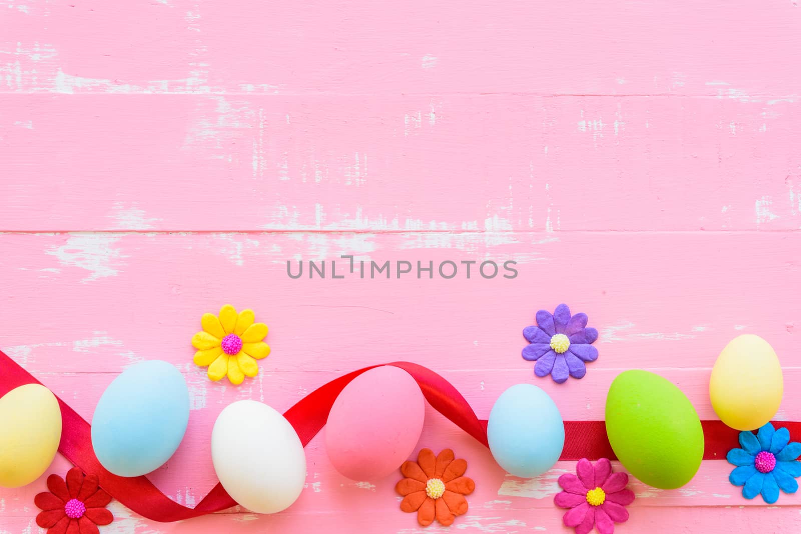 Row Easter eggs with colorful paper flowers on bright pink and white wooden background.