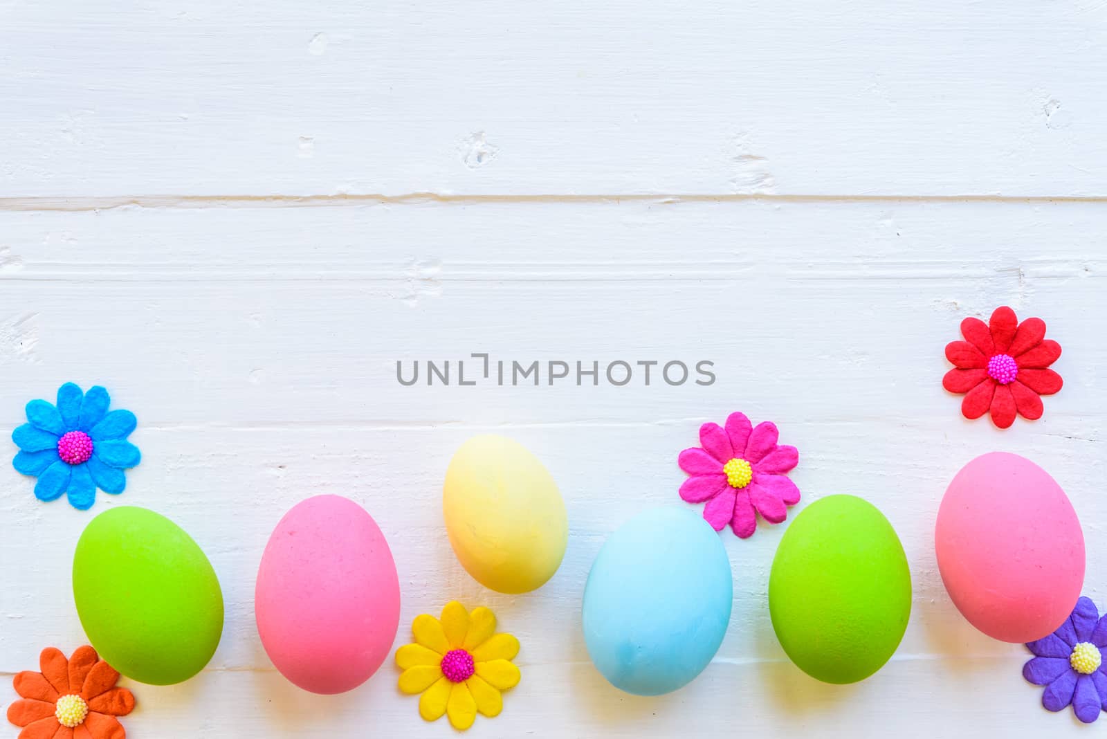 Row Easter eggs with colorful paper flowers on bright pink and white wooden background.