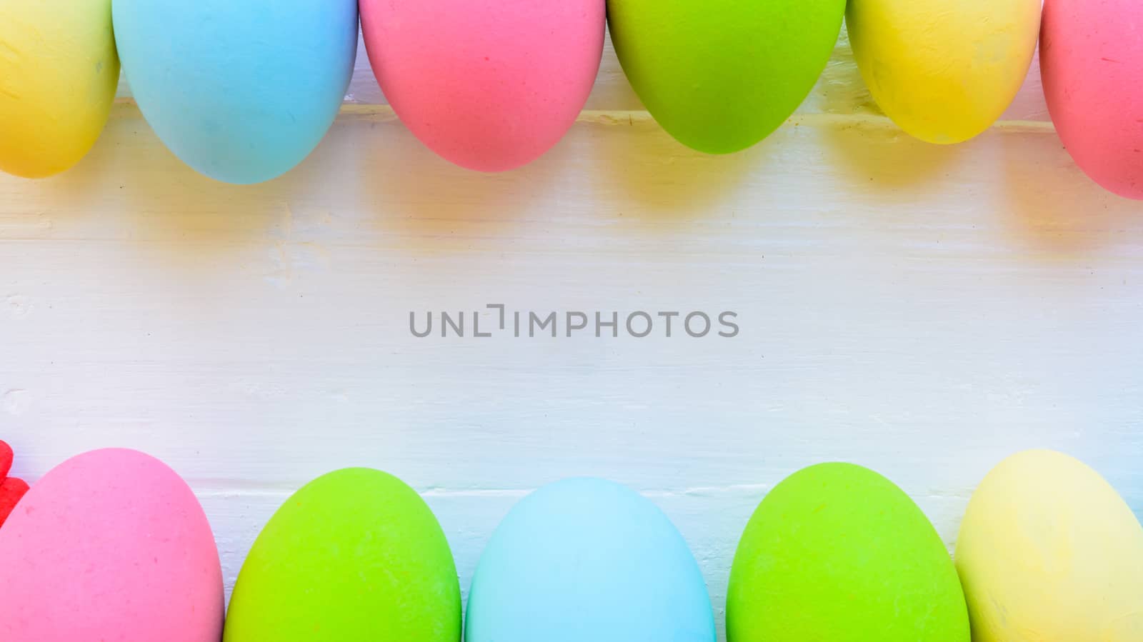 Row Easter eggs with colorful paper flowers on bright pink and white wooden background.