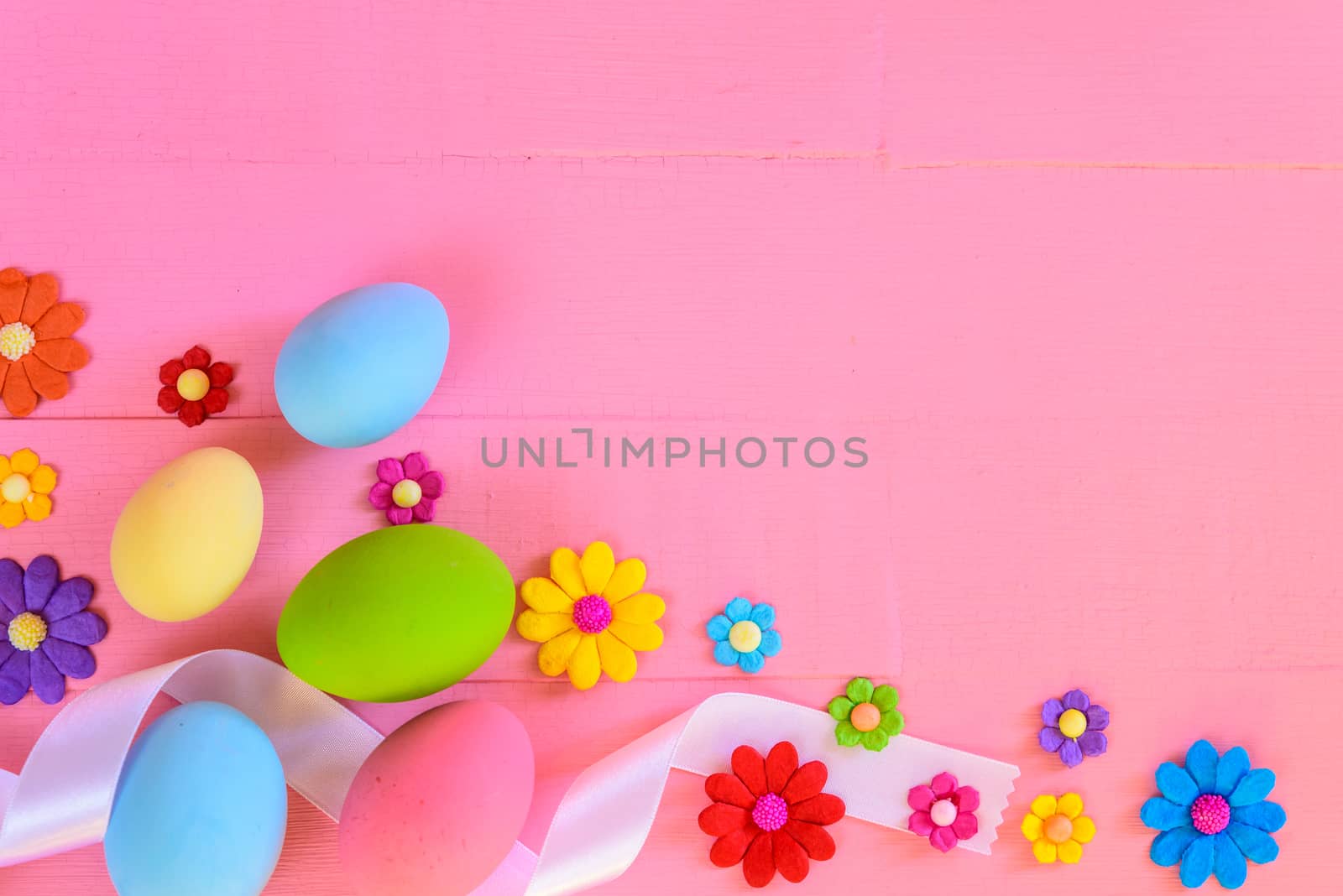 Easter eggs with colorful paper flowers on bright pink wooden background.