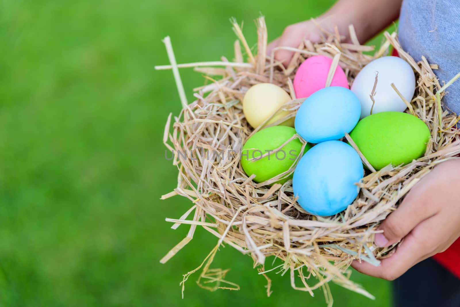 A kid holding Colorful of Easter eggs in nest on grass green background.