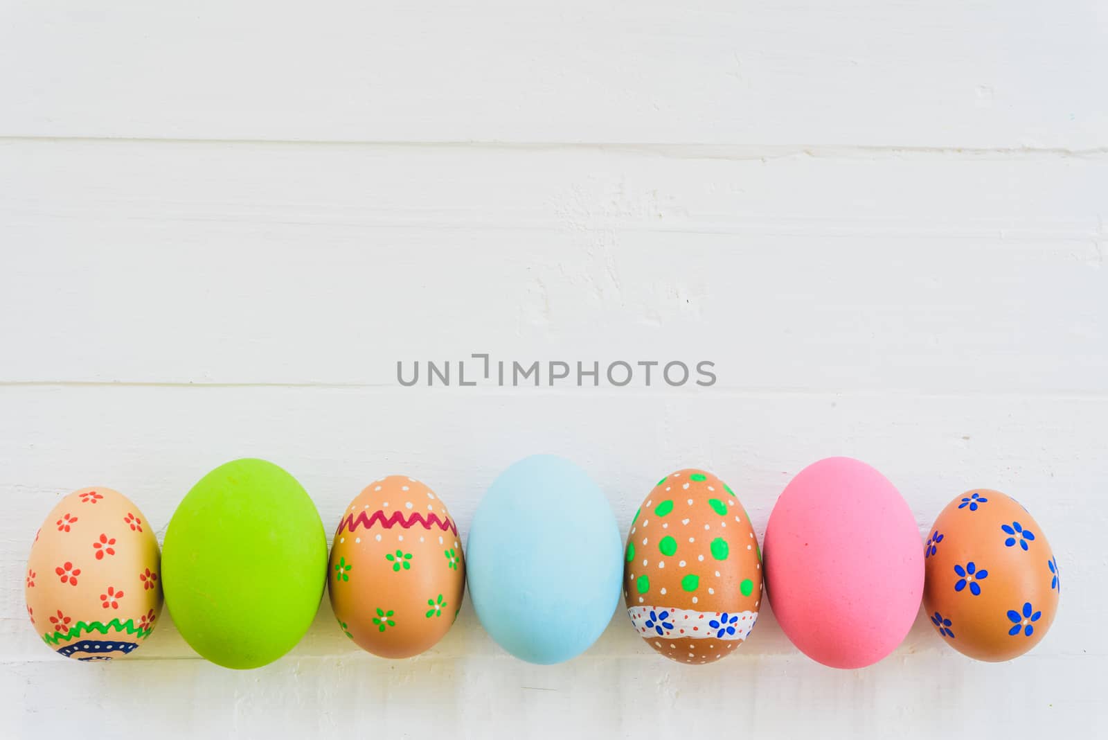 Happy easter! Row Colorful Easter eggs with colorful paper flowers on white wooden background.