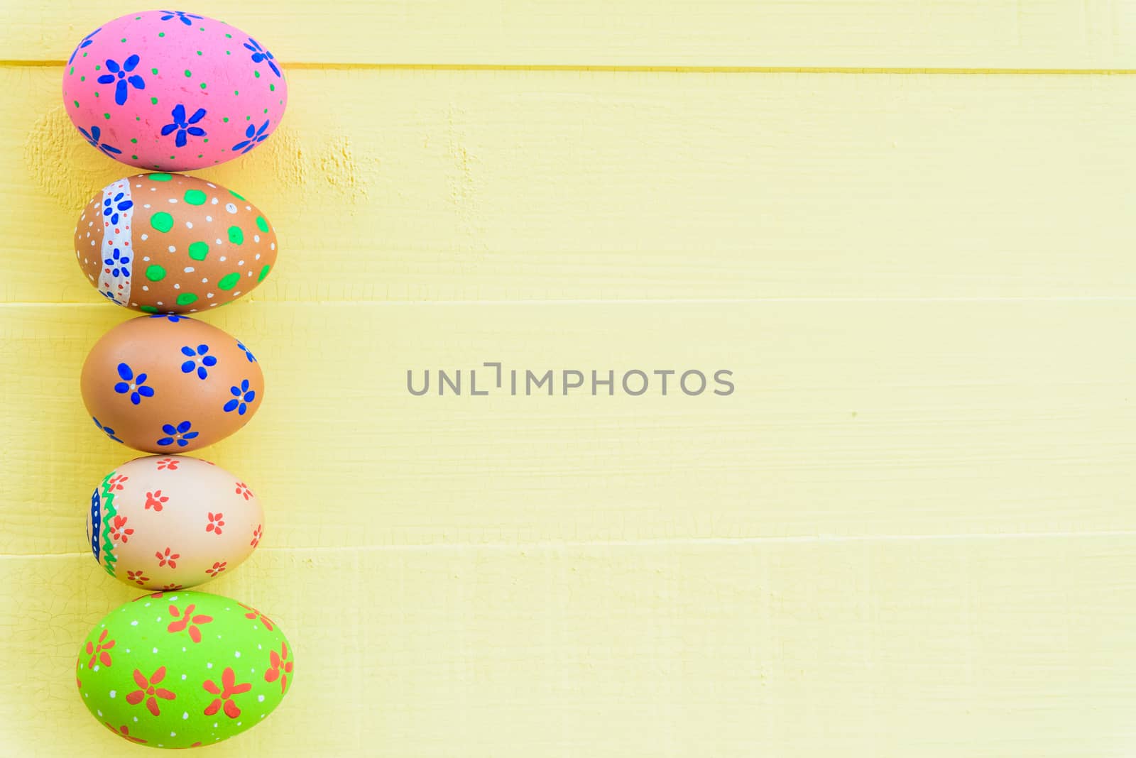 Happy easter! Row Colorful Easter eggs with colorful paper flowers on bright yellow wooden background.